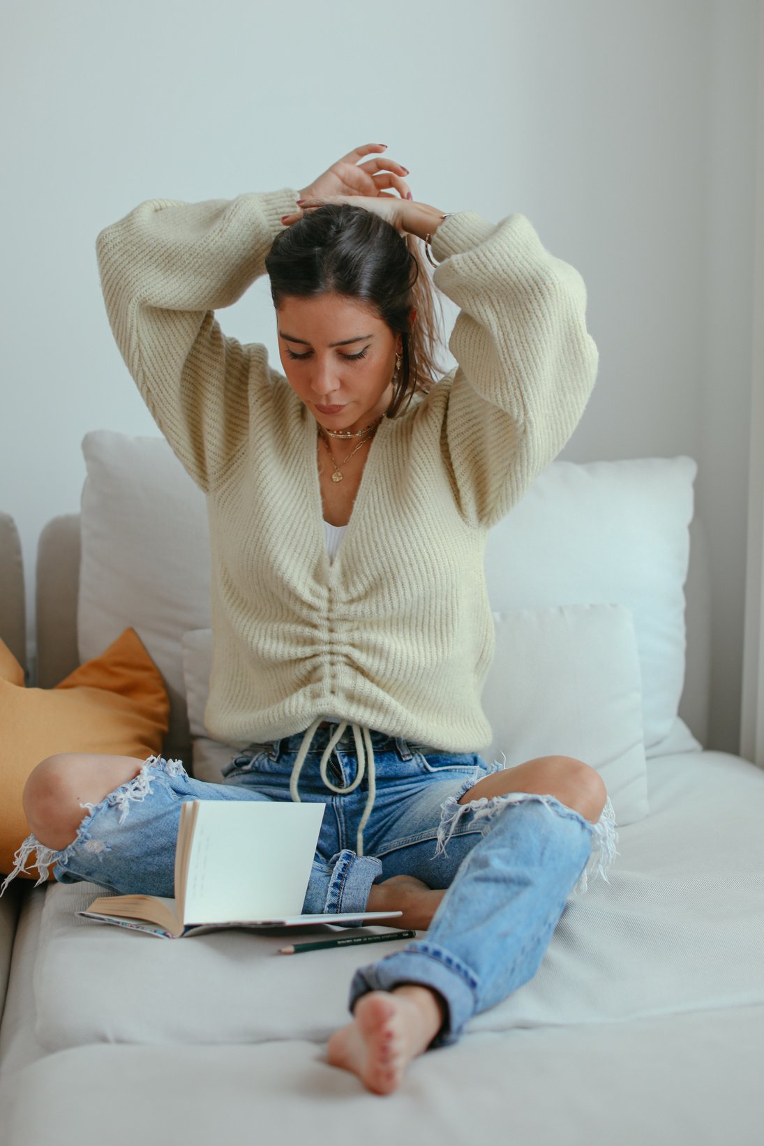 Woman Sitting on Sofa While Tying Her Hair